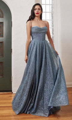 A woman stands indoors near a green door and window, wearing the Draped-Bodice Long Glitter A-Line Prom Dress CD252 in sparkly blue with thin straps and a corset bodice.