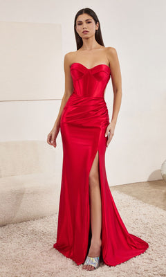 A woman stands indoors wearing the Sheer-Side Strapless Long Prom Dress CD273—an elegant, form-fitting red satin gown with a thigh-high slit and silver heels.
