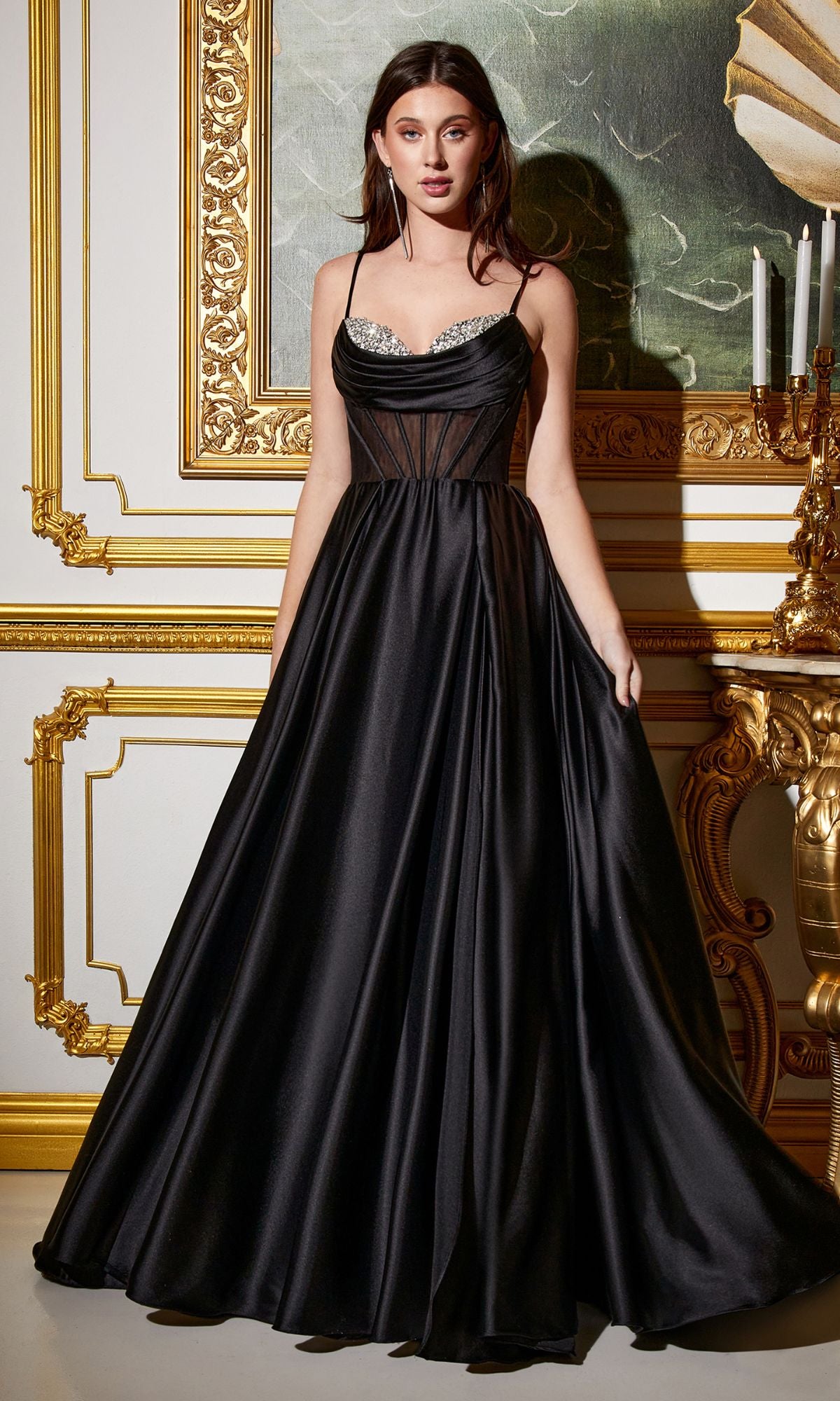 A woman wearing the Sheer-Corset Long A-Line Prom Dress CD276 stands in an ornate, gold-trimmed room. The gown features a structured bodice and rhinestone details for an elegant, formal look.