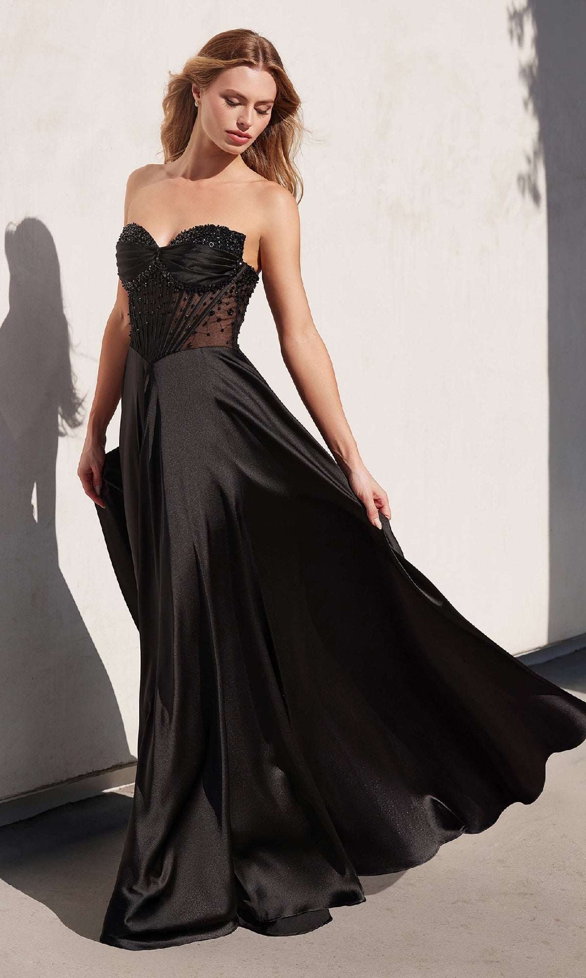 A woman stands against a light-colored wall wearing the Ladivine CD297, a strapless long A-line prom dress with a fitted beaded bodice and flowing skirt.