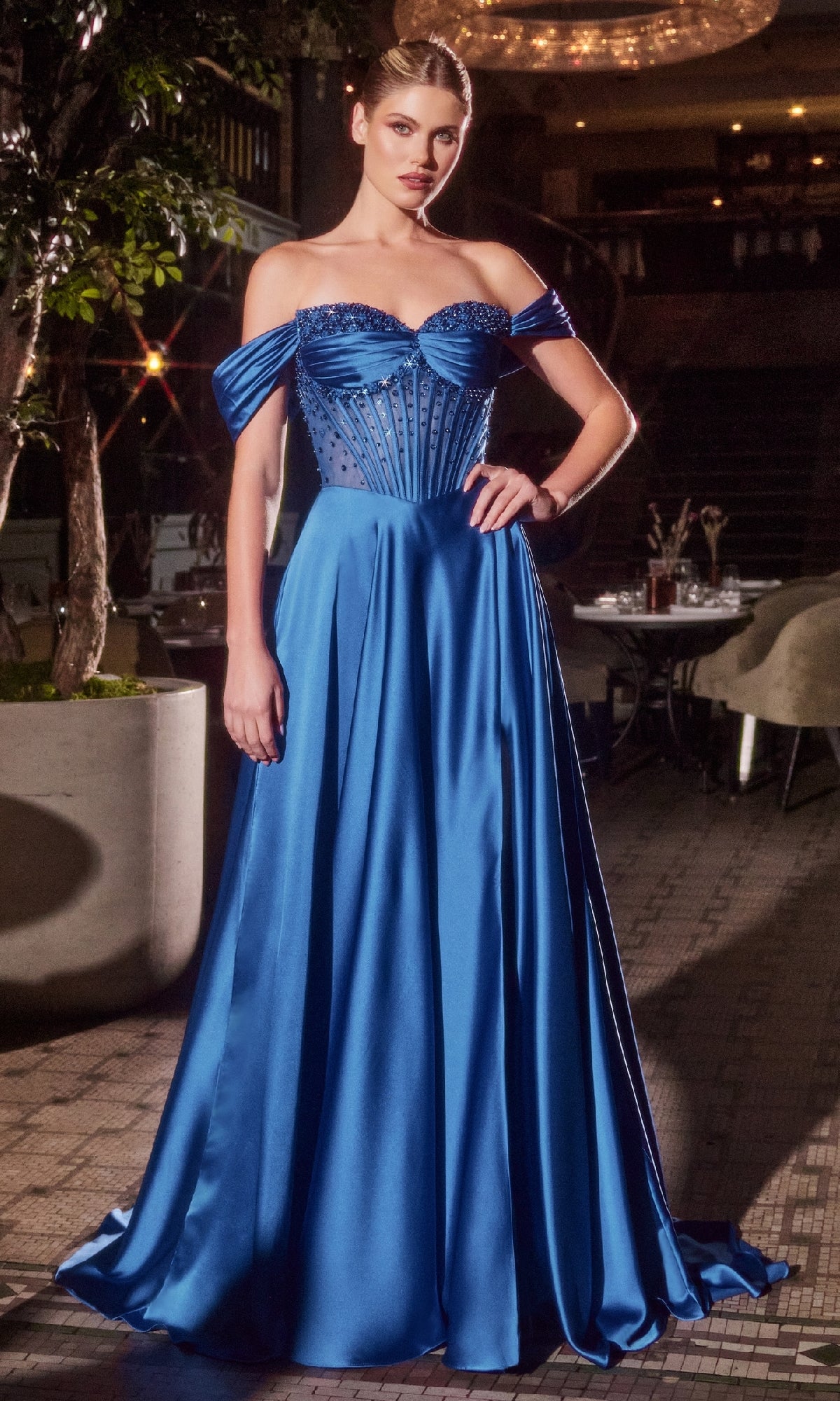Indoors, a woman wears the Ladivine CD297—a strapless, floor-length A-line prom dress in royal blue satin with a beaded corset bodice and flowing skirt.
