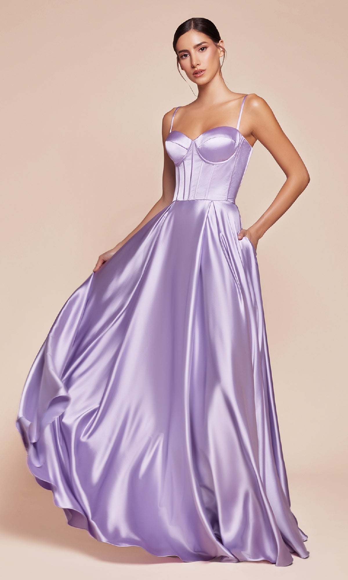 A woman in the Long Sweetheart A-Line Prom Dress: Ladivine CD337, featuring a shiny lavender satin corset bodice with thin straps, stands against a plain beige background, holding the skirt out to the side.