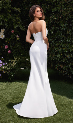 A woman in the Strapless Off-White Prom Gown: Ladivine CD355W stands on grass outdoors, facing slightly away, with greenery and flowers in the background.