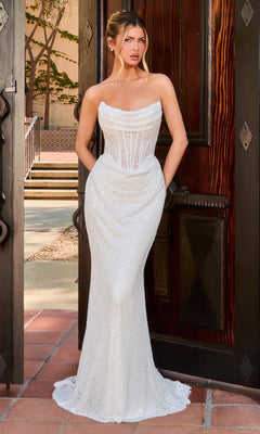 A woman in the Ladivine CD396W long prom dress, featuring an off white, form-fitting gown with a sheer corset bodice, stands in an open doorway on a sunny day.