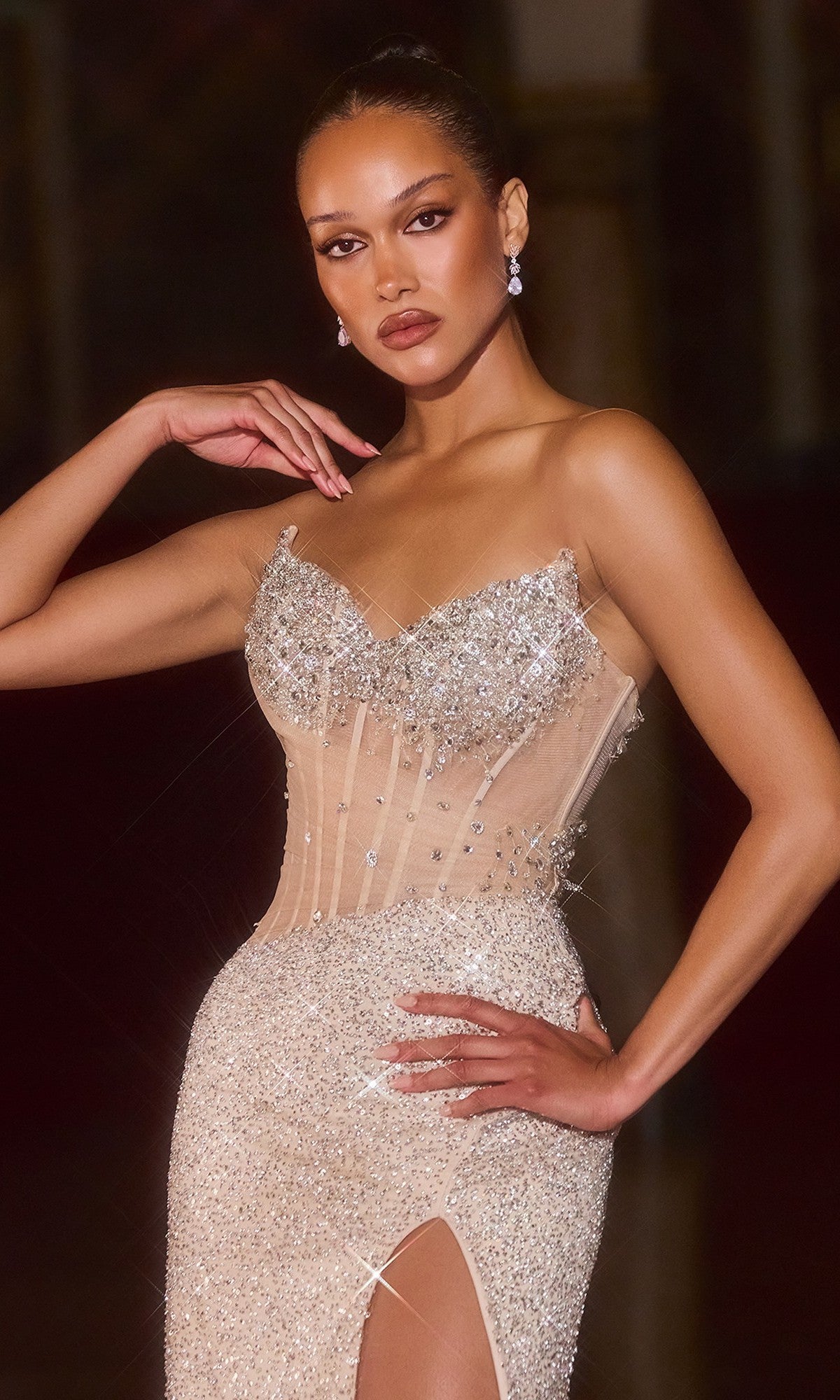 A woman poses in the Ladivine CD404 Long Prom Dress, a fitted strapless gown with jeweled details, a thigh-high slit, and a sheer corset bodice—one hand on her hip, the other raised near her head.