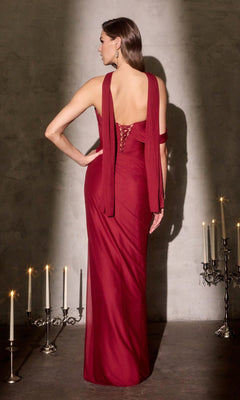 A woman in the Ladivine CD406 Long Prom Dress, featuring a floor-length, backless red design with an elegant lace-up back, stands facing away as flowing fabric drapes near glowing candelabras beside a textured wall.