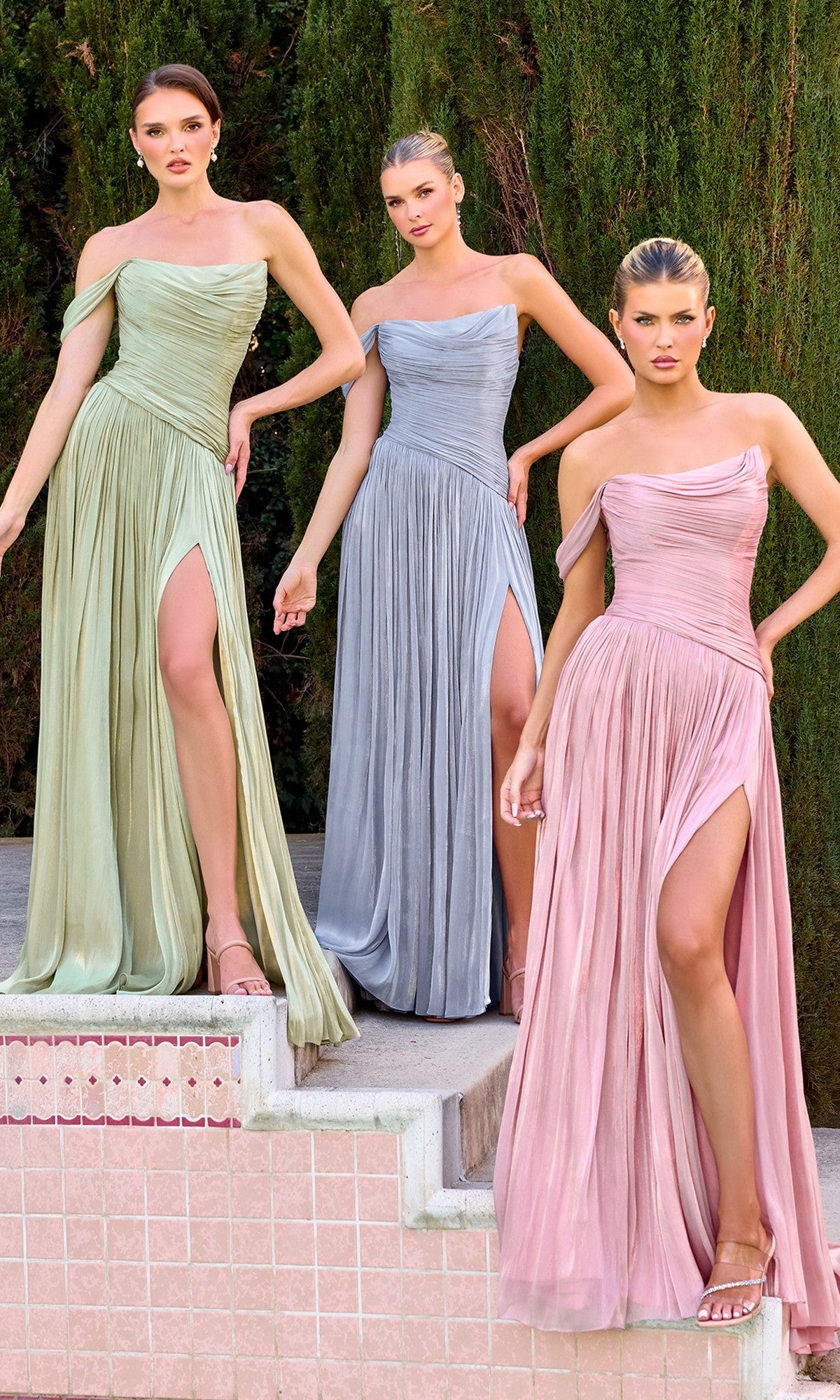 Three women pose on outdoor steps in pastel green, blue, and pink Ladivine CD409 long prom dresses with pleated chiffon fabric, high slits, and asymmetrical necklines. Lush trees provide a scenic backdrop.