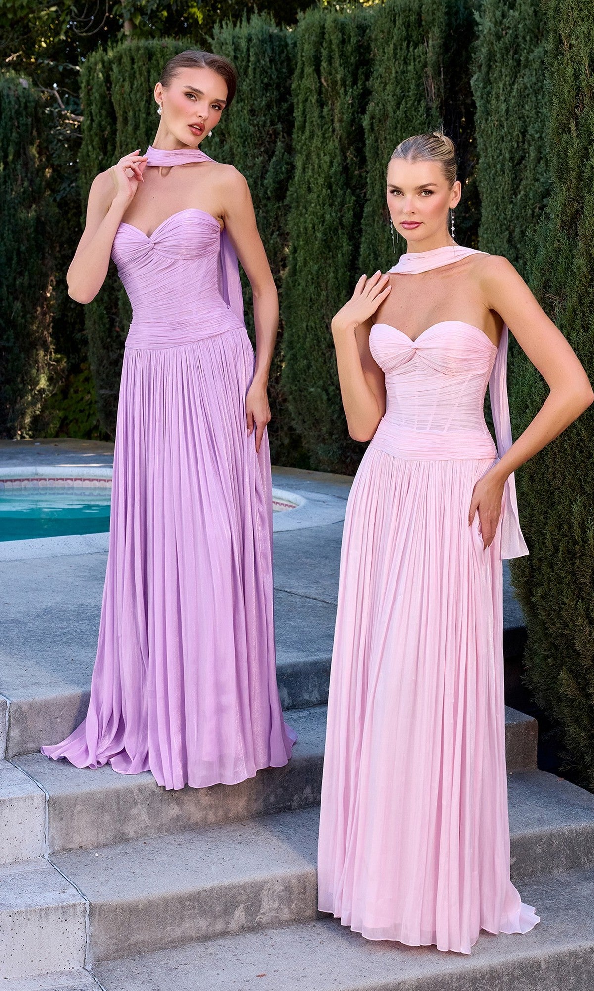 Two women stand outdoors near a pool, wearing the Ladivine CD414 long prom dress in light purple and pink with matching sheer scarves. Tall green hedges are in the background.