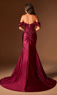 A woman wears the Ladivine CD656 long prom dress, featuring an off-the-shoulder satin design with a fitted bodice, lace-up back, gathered lower back detail, and floor-length burgundy skirt against a brown background.
