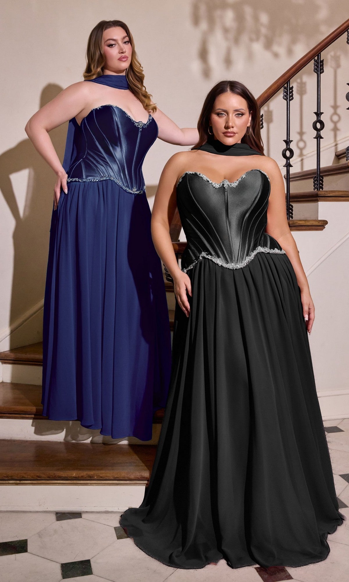 Two women stand on a staircase, each wearing the Long Plus-Size Prom Dress: Ladivine CD668C in navy. The strapless gown features a metallic corset bodice and flowing chiffon skirt, making it a stunning plus size prom dress option.