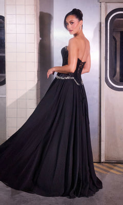 Wearing the Ladivine CD668 Long Prom Dress, a woman in a strapless black evening gown with a satin corset bodice stands in front of tiled wall and metal subway doors, looking over her shoulder.