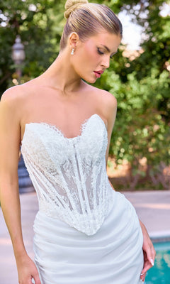 Wearing the Ladivine CD683W long wedding dress, a woman in a strapless corset gown with a lace-embellished chiffon skirt stands outdoors, her hair styled in a neat bun as she looks down.
