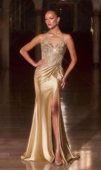 A woman stands in an ornate hallway wearing the Ladivine CD690 Sheer-Corset Long Halter Prom Gown, featuring a gold satin finish, embellished corset-style bodice, thigh-high slit, and strappy heels for a glamorous look.