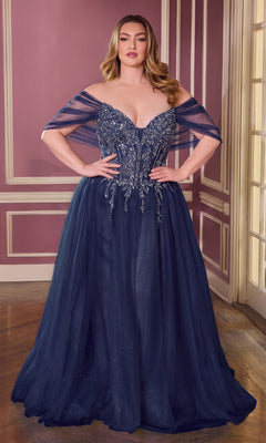 A woman stands in a room with pink walls and white trim, wearing the Plus-Size Glitter Prom Ball Gown (CLCD721C) in navy. The off-the-shoulder, floor-length dress features sparkling beaded embellishments.