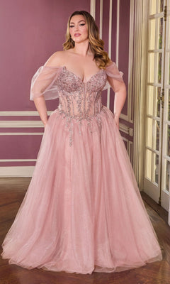 A woman stands indoors wearing the Ladivine CD721C, a long, plus-size mauve prom dress featuring an embellished corset bodice and sheer tulle off-the-shoulder sleeves.