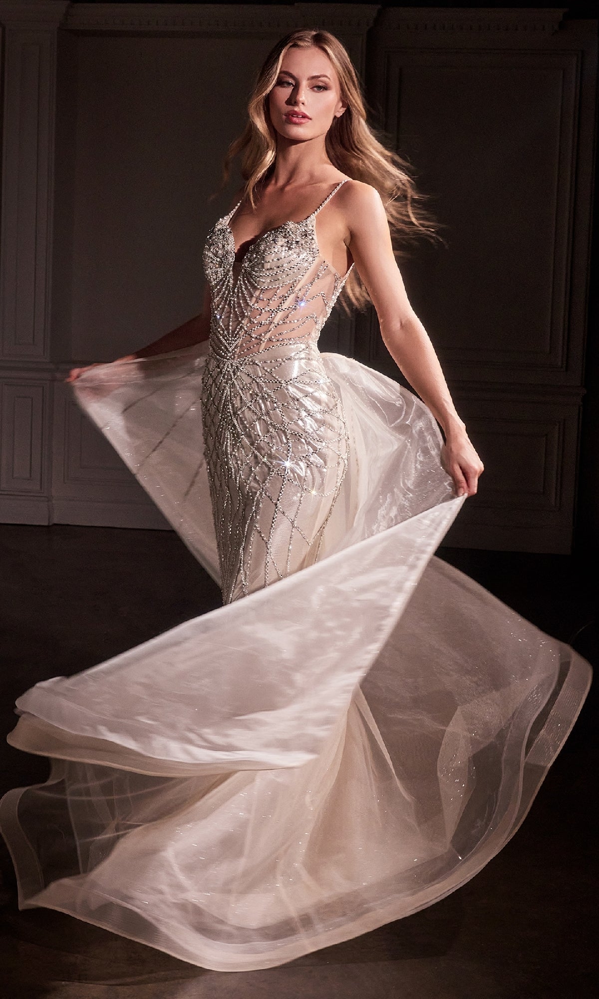 Woman wearing the Ladivine CD763 Overskirt Long Glitter Prom Dress, featuring a fitted, sleeveless beaded design with sheer panels and a flowing removable overskirt, twirls indoors as her glamorous formal gown swirls around her.