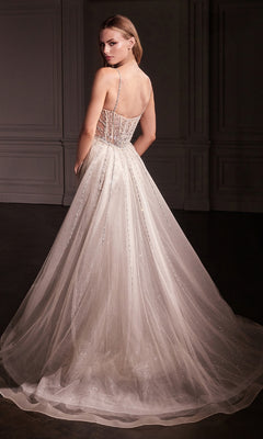 A woman in the Overskirt Long Glitter Prom Dress Ladivine CD763, featuring a floor-length shimmering design with a sheer corset-style back and thin straps, stands in an elegant, dimly lit room.