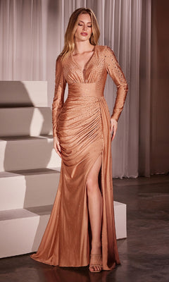 A woman stands indoors wearing the Long Sleeve Long Beaded Prom Dress (CLCD788), a copper formal gown featuring long sleeves, a deep V-neckline, ruched details, a thigh-high slit, and paired with matching heels.