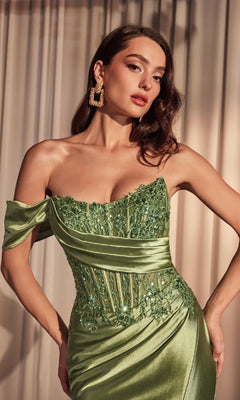 Woman in the Ladivine CD804 One-Shoulder Long Prom Dress—an elegant fitted green satin gown with an embroidered corset bodice and large square earrings—stands before beige curtains.