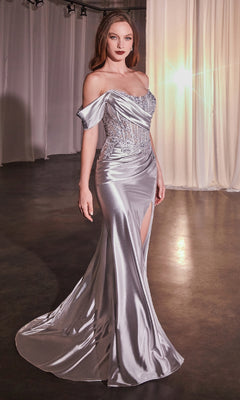A woman in the Ladivine CD804, a floor-length silver one-shoulder prom dress with an embroidered corset bodice and thigh-high slit, stands indoors on a dark floor with sheer curtains and bright light behind her.