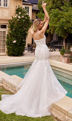 A woman in the Puff Sleeve Mermaid Wedding Gown CD858W poses by a swimming pool, arms raised, in an outdoor garden setting.