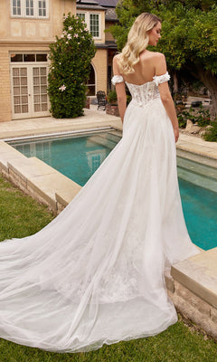 A woman in the 3D Floral Lace Wedding Gown CD861W with a removable tulle overskirt stands by a pool in a garden, facing away from the camera.