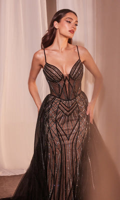 A woman wearing the Beaded Overskirt Long Formal Prom Dress CD863, featuring a sheer black design with intricate geometric beadwork, thin straps, and a fitted bodice, stands in front of light-colored curtains.