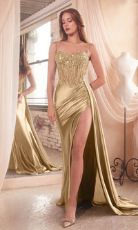 Woman wearing a long gold prom dress with a sheer corset bodice standing in front of a mirror with draped curtains.