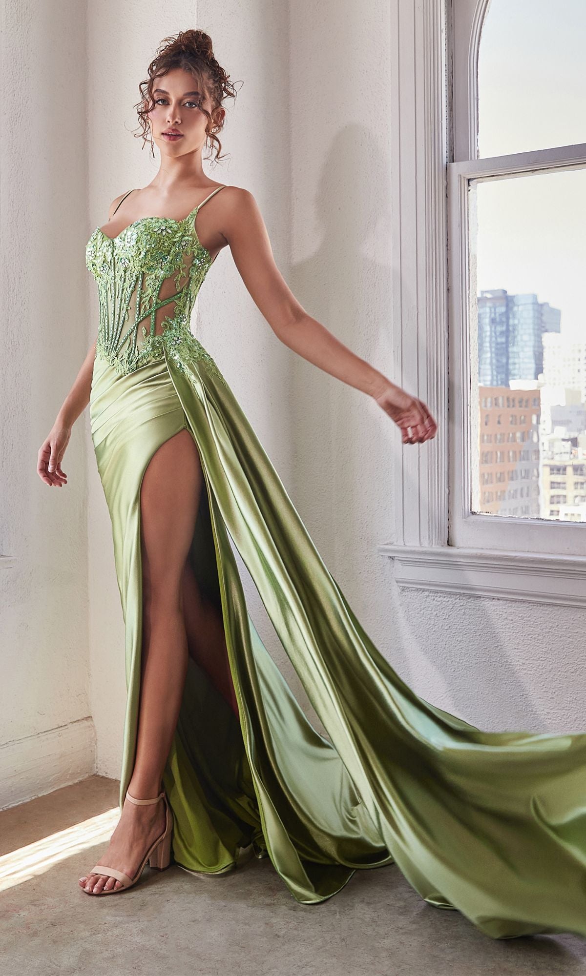 A model wearing a long sweetheart green prom dress with a sheer embellished bodice and a side slit.