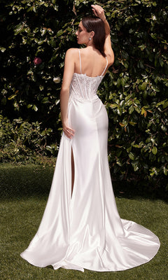 A woman stands outdoors on grass, facing away, wearing the Corset White Satin Formal Dress: Ladivine CD868W with a lace bodice, thin straps, high slit, and greenery in the background.