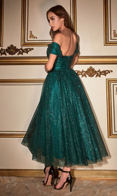 A woman in the Glitter Tea-Length Off-Shoulder Hoco Dress CD870 and black heels stands before an ornate cream and gold wall, glancing over her shoulder.
