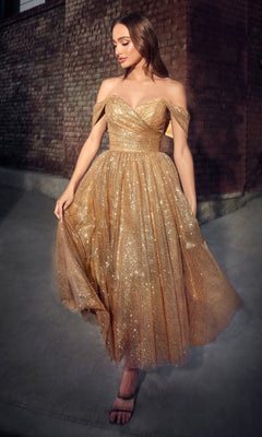 A woman stands outdoors in the Glitter Tea-Length Off-Shoulder Hoco Dress CD870—a sparkling gold, knee-length design with fitted bodice and flared skirt—stylishly paired with black strappy heels.