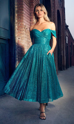 A woman stands by a brick building in the Glitter Tea-Length Off-Shoulder Hoco Dress CD870—a shimmery teal midi dress with a full skirt—paired with strappy heels.