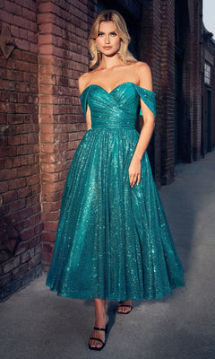 A woman stands outdoors by a brick wall, wearing the Glitter Tea-Length Off-Shoulder Hoco Dress CD870 in teal with sparkly details, featuring a knee-length full skirt and paired with black strappy heels.