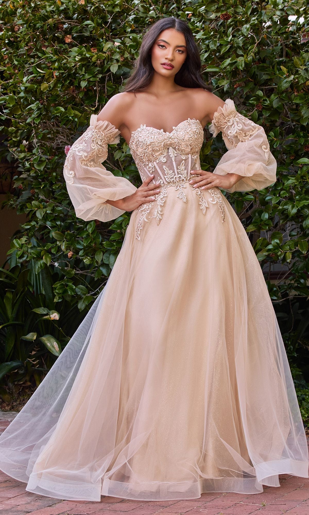 A woman stands outdoors in the Strapless Puff-Sleeve Long Prom Dress CD948, featuring a blush sweetheart neckline, sheer corset bodice with floral appliques, voluminous tulle skirt, and removable puff sleeves for a romantic look.