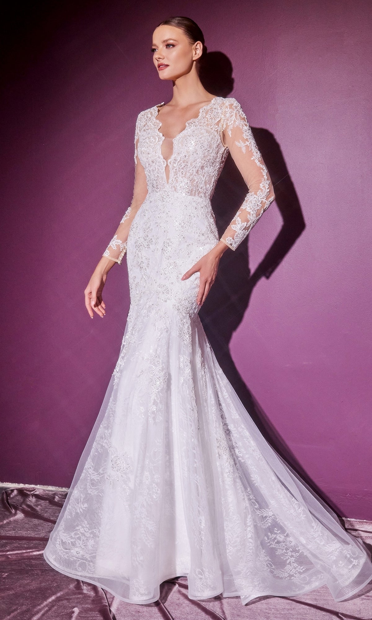 A woman stands against a purple wall wearing the Long Sleeve Long White Wedding Dress CD951W—an elegant bridal gown with a fitted bodice and flared skirt.