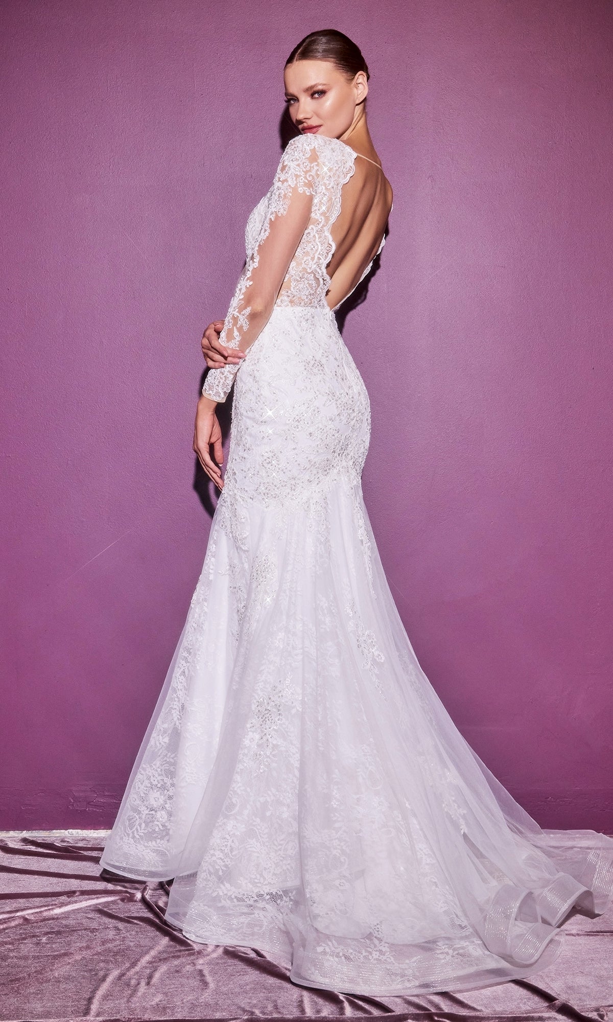 A woman in the Long Sleeve Long White Wedding Dress CD951W with lace, a mermaid silhouette, and open back stands against a purple wall, looking over her shoulder.