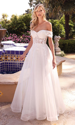 A woman poses outdoors by a tiled fountain in the Sheer-Bodice Long White Prom Ball Gown CD961W, an off-the-shoulder dress with a lace bodice and flowing tulle skirt—ideal for anyone seeking a romantic long A-line formal gown.