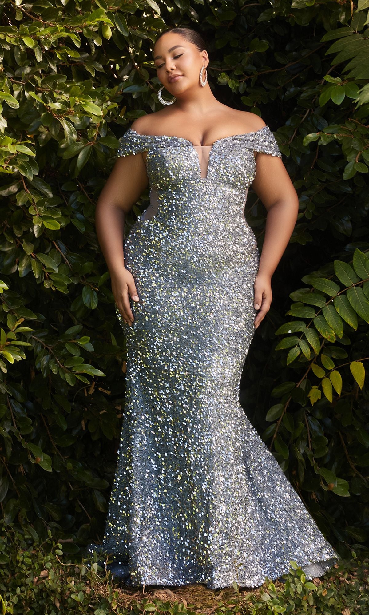 A woman stands outdoors before green foliage, wearing the Plus-Size Sequin Mermaid Prom Dress CD975C featuring an off-the-shoulder neckline, fitted bodice, and flared mermaid skirt.
