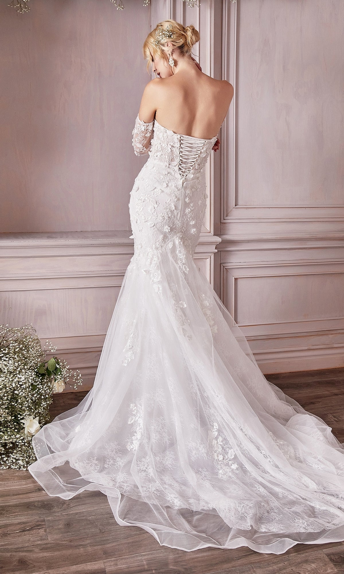 A woman stands with her back to the camera in an elegantly decorated room, wearing the Long White Strapless Bridal Gown CD977W, featuring embroidered floral designs, a fitted bodice, and a mermaid skirt.