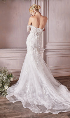 A woman stands with her back to the camera in an elegantly decorated room, wearing the Long White Strapless Bridal Gown CD977W, featuring embroidered floral designs, a fitted bodice, and a mermaid skirt.