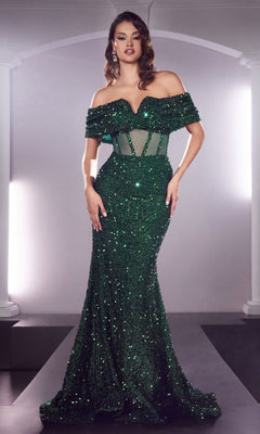 A woman stands in a well-lit room wearing the Sheer-Waist Off-Shoulder Sequin Formal Dress CD985, a fitted floor-length green mermaid gown with sequins and sheer waist paneling.