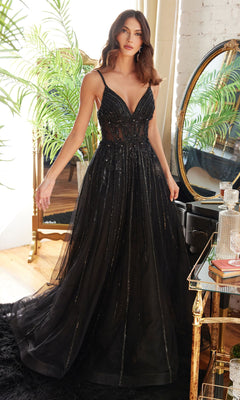 A woman stands indoors among elegant decor, wearing the Long A-Line Prom Dress with Sheer Bodice CD994—a floor-length black gown featuring a sleeveless design, deep V-neck, and sheer bodice.