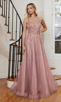 A woman poses indoors on hardwood flooring by a curved staircase, wearing the Long A-Line Prom Dress with Sheer Bodice CD994, a sleeveless, floor-length pink gown adorned with lace and sequin details.