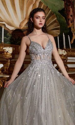 A woman in the Long A-Line Prom Dress with Sheer Bodice CD994, featuring silver sparkle and intricate beading, stands before a classical painting and ornate candlelit decor, gracefully holding the sides of her gown.