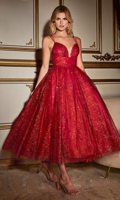 A woman stands indoors wearing the Tea-Length Glitter Party Dress CD996T in deep red with a full skirt and spaghetti straps, paired with clear high-heeled shoes.