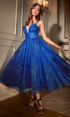 Woman in a glittery blue Tea-Length Glitter Party Dress CD996T with spaghetti straps stands indoors by a white wall and chandelier, holding the sides of her A-line party dress.