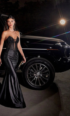 A woman wearing the Sheer-Bodice Strapless Long Prom Dress CDS419 stands beside a luxury black car at night, highlighted by bright lighting in the background.