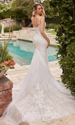 Wearing the Chantilly-Lace Long Off-White Formal Dress CDS432W, a woman stands by a pool in a beautiful garden, showcasing the gown's corset-style waist and long train as she faces away from the camera.