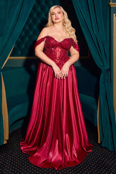 A woman stands before green velvet curtains, wearing the Off-the-Shoulder Prom Ball Gown: Ladivine CDS525, featuring a fitted, embellished bodice and a flowing red satin skirt.